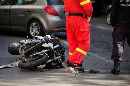 damaged motorcycle on street with vehicle in background and worker in orange uniform